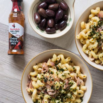 Pasta with bacon and mushrooms in white bowl and black olives on the side