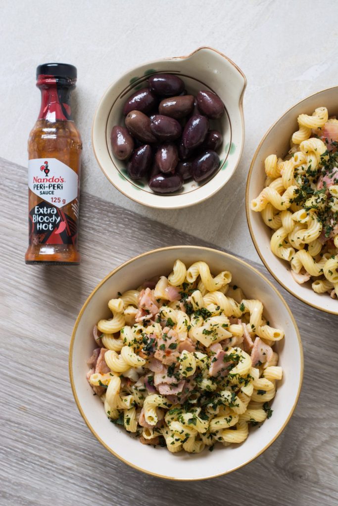 Pasta with bacon and mushrooms in white bowl and black olives on the side