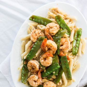 Pasta with prawns and snow peas on white plate