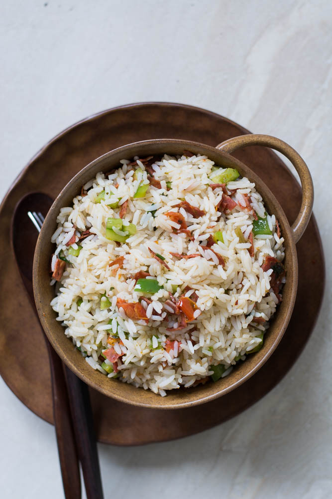 Stir fried rice with salami, sun dried tomatoes in brown bowl