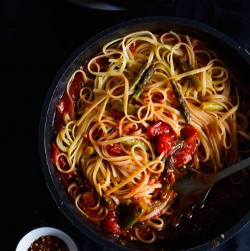 Pasta tossed with tomato sauce and asparagus in a black pan