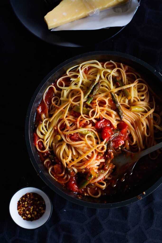 Pasta tossed with tomato sauce and asparagus in a black pan