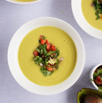 Avocado soup topped with spicy salsa served in white bowl