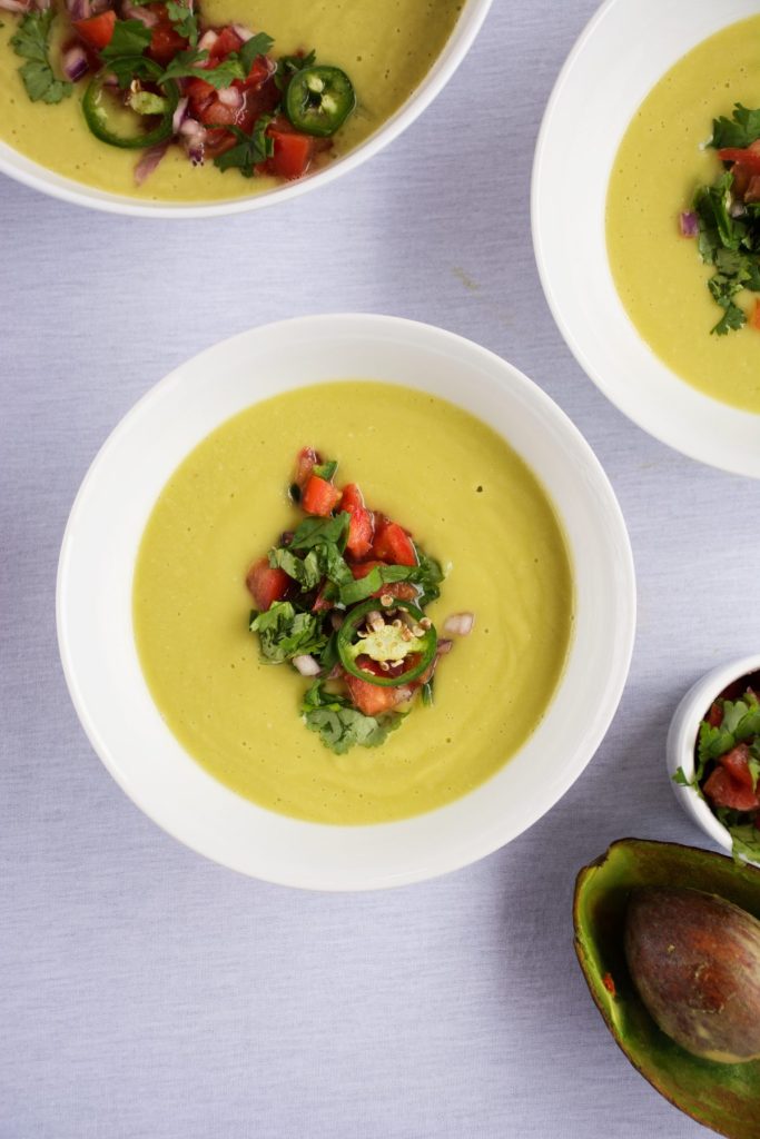 Avocado soup topped with spicy salsa served in white bowl