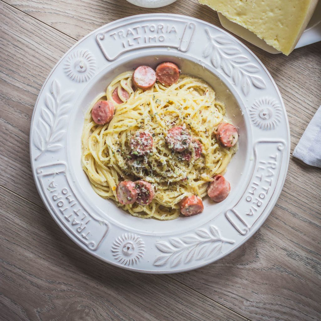 Spaghetti with sliced sausages in white sauce in white bowl