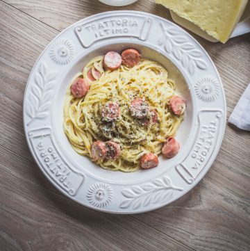 Spaghetti with sliced sausages in white sauce in white bowl