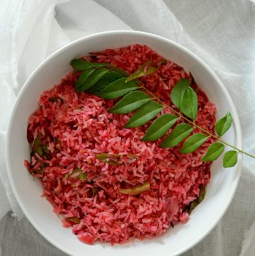 Beetroot rice garnished with curry leaf sprig in white bowl