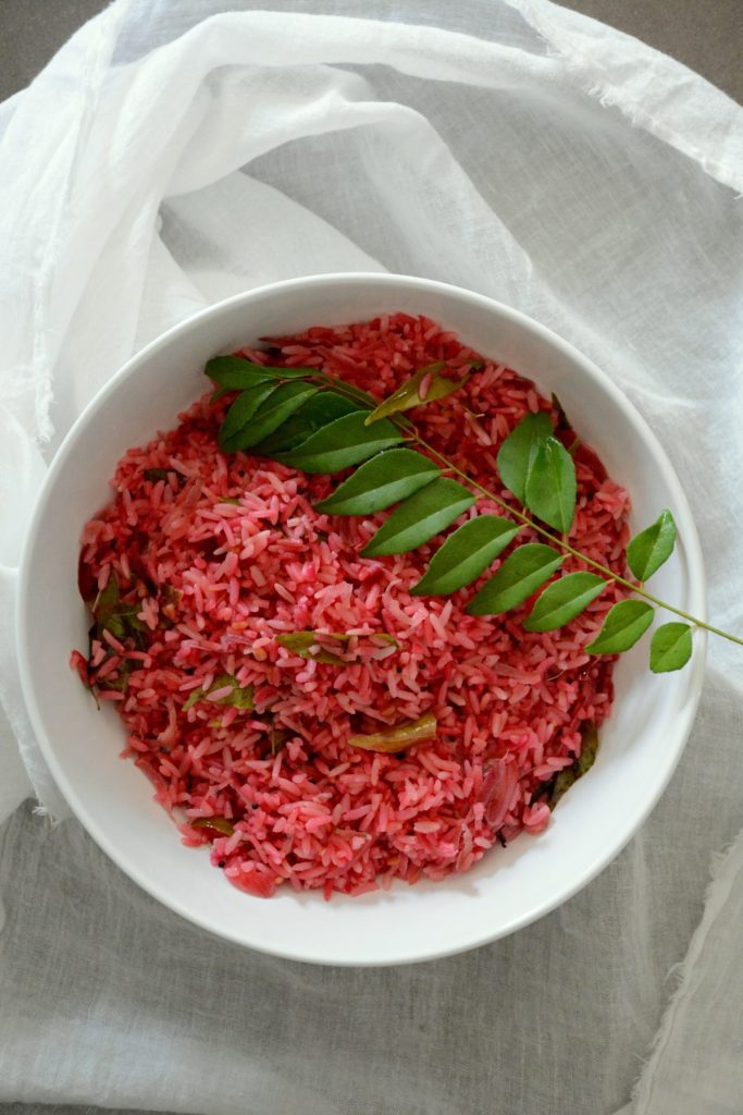 Beetroot rice garnished with curry leaf sprig in white bowl