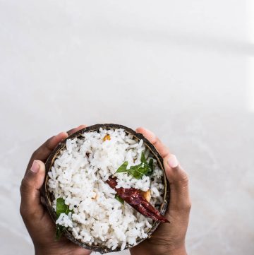 Hand holding coconut rice inside coconut shell