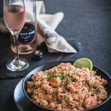 Prawn pilaf in black bowl with a glass of rose on the side