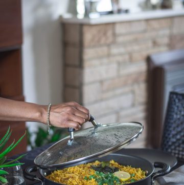 Hand lifting lid of large pan with chickpea biryani on dining table