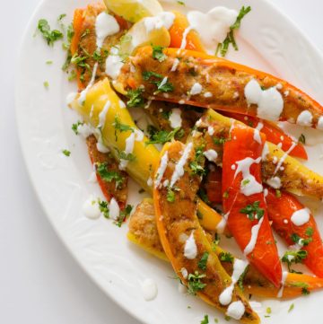 Stuffed yellow and orange chilli peppers drizzled with yoghurt and served on white plate
