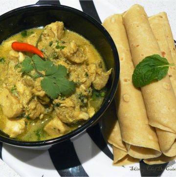 Malaysian style chicken curry in black bowl with flatbreads on the side
