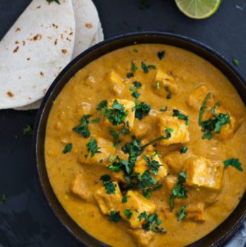 Indian cottage cheese curry served in black bowl with flatbreads and salad on the side