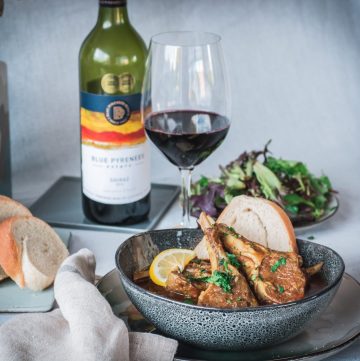 lamb chops curry in blue bowl with a glass of red wine and salad on the side