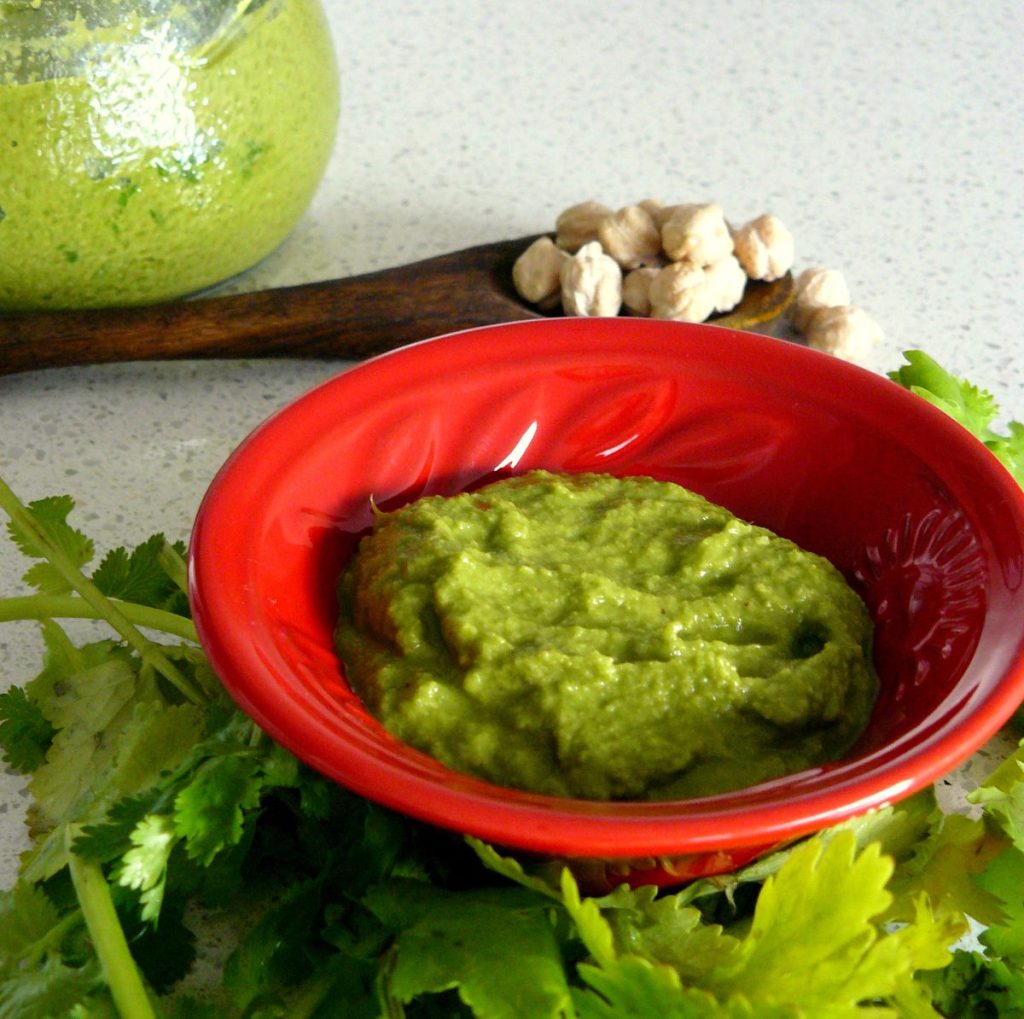 Coriander chickpea chutney in red bowl with fresh coriander leaves on the side