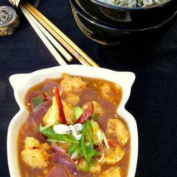 Indo Chinese style chicken garnished with spring onions and dried chillies served in white bowl