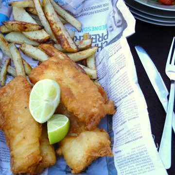 Batter fried fish with chips and lime wedges served in newspaper