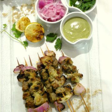 Grilled lamb skewers served with lime wedges, pickled onions and mint chutney