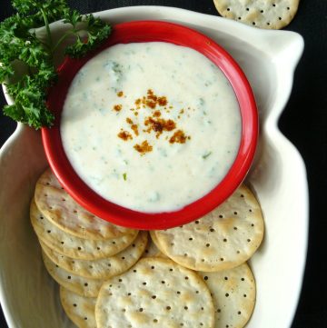 Parsley yoghurt dip in red bowl with crackers on the side
