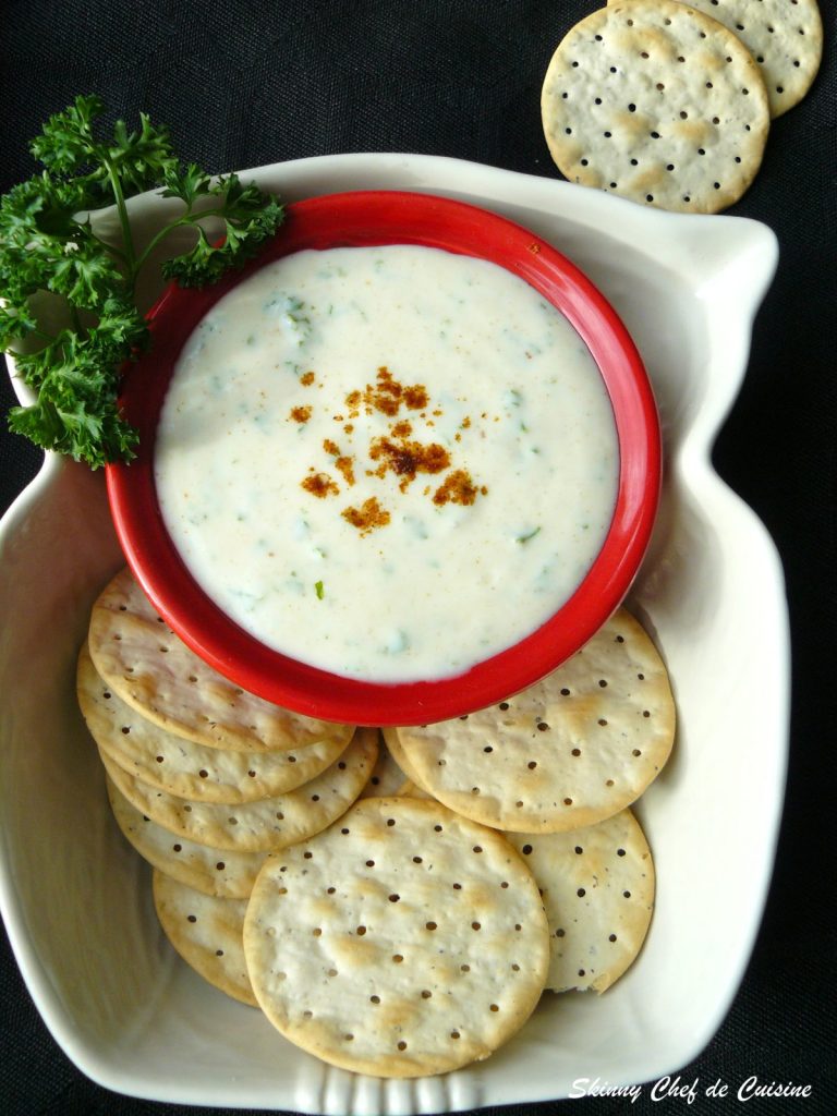 Parsley yoghurt dip in red bowl with crackers on the side