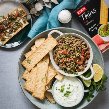 Moroccan lamb salad in white bowl along with crackers and yoghurt dip