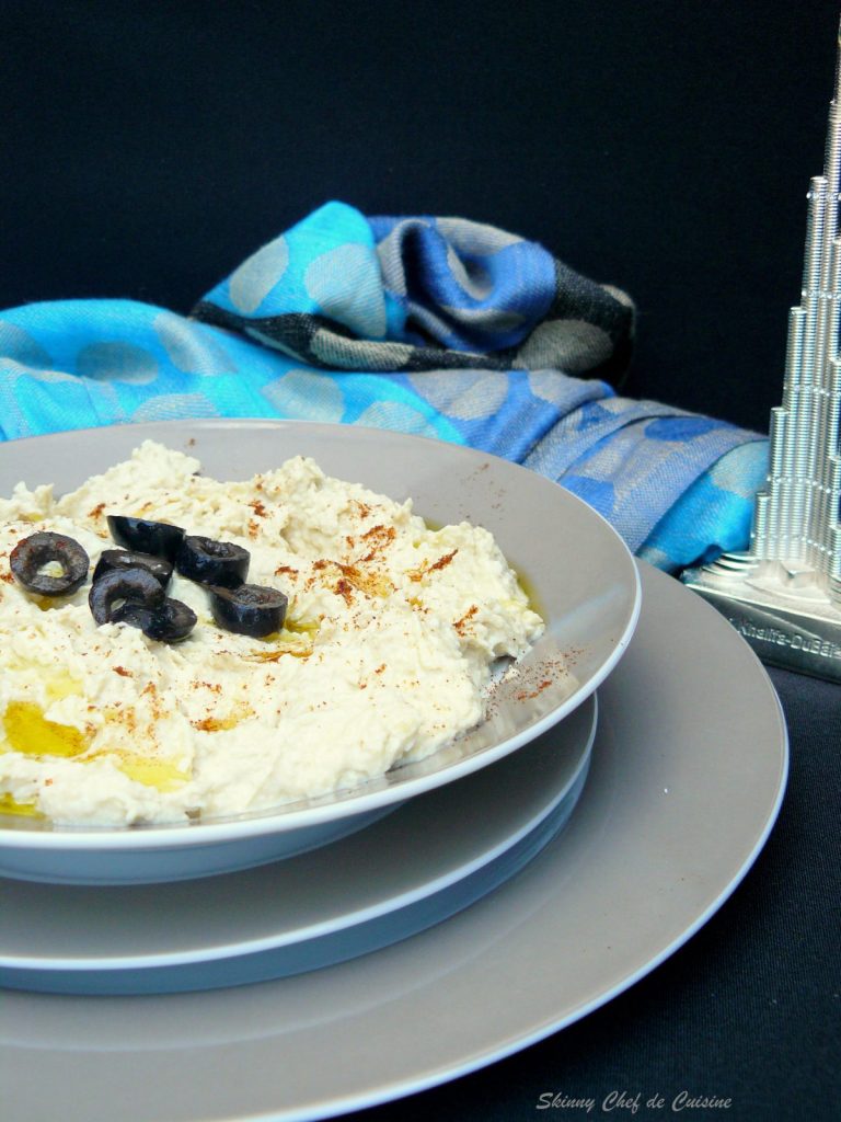 Hummus in a grey bowl garnished with olive oil and black olives
