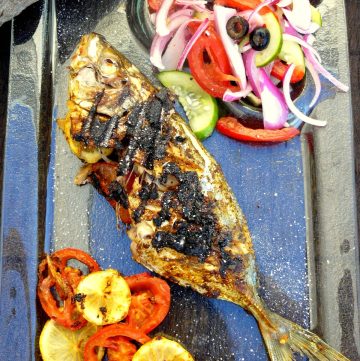 Grilled whole fish with lemon slices and salad