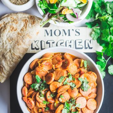 Indian style sausage curry in white bowl with salad and flatbread on the side