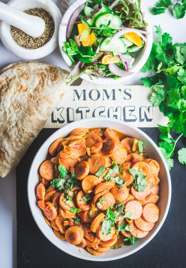 Indian style sausage curry in white bowl with salad and flatbread on the side