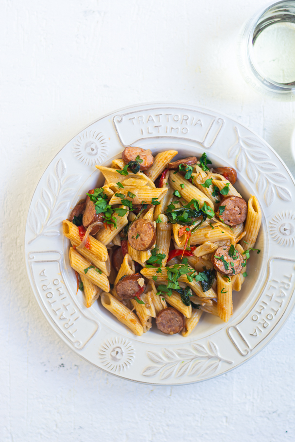 Penne pasta with sausages and tomatoes in white bowl