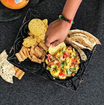 Hand dipping cracker into mango salsa