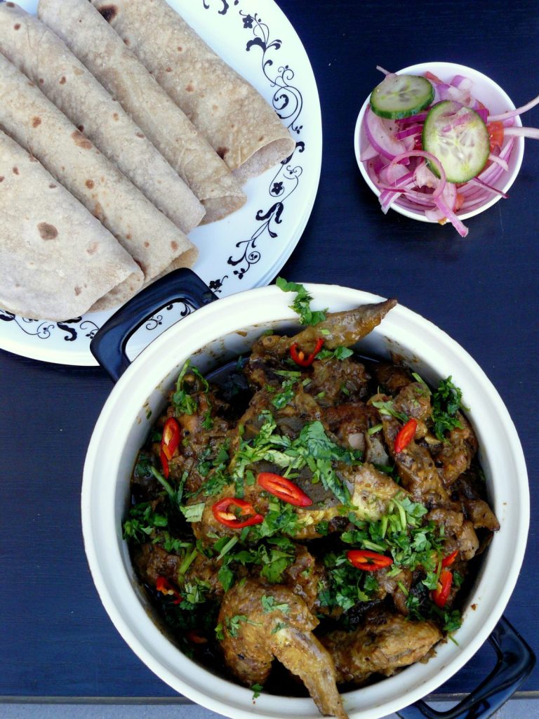 Indian chicken wings curry garnished with coriander leaves and red chillies, salad and flatbreads