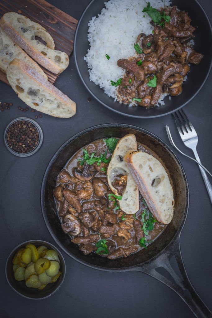Beef stroganoff with bread in a cast iron pan and beef stroganoff served with rice in a black bowl