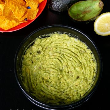 Guacamole in black bowl with tortilla chips on the side