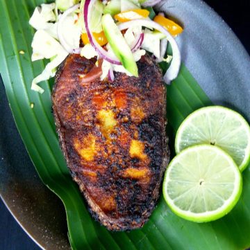 Fried salmon steak served on banana leaf with salad and lime slices