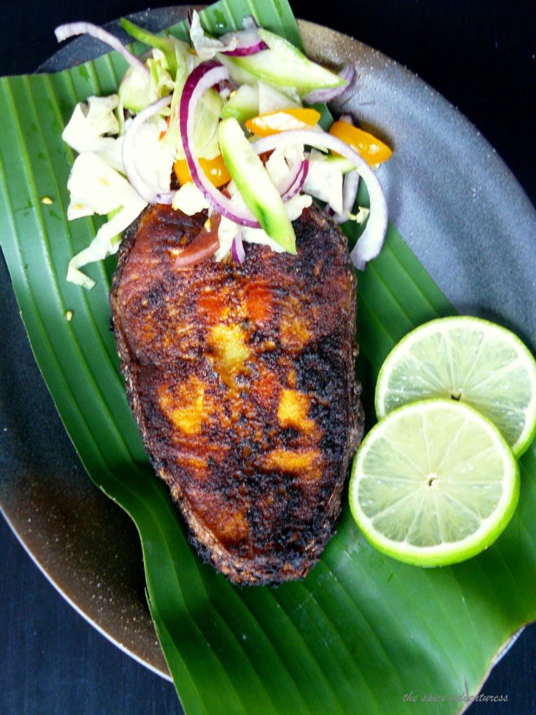 Fried salmon steak served on banana leaf with salad and lime slices