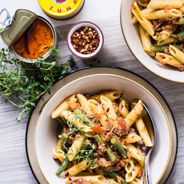 Pasta with tuna in white bowl and two canned tuna tins on the side