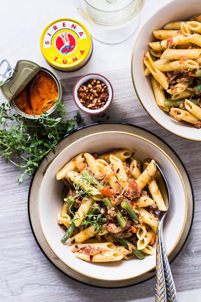 Pasta with tuna in white bowl and two canned tuna tins on the side