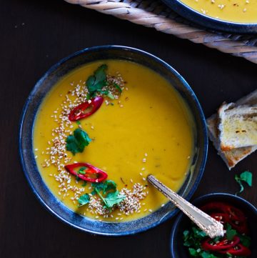 Pumpkin and potato soup garnished with sesame seeds and red chillies served in black bowl