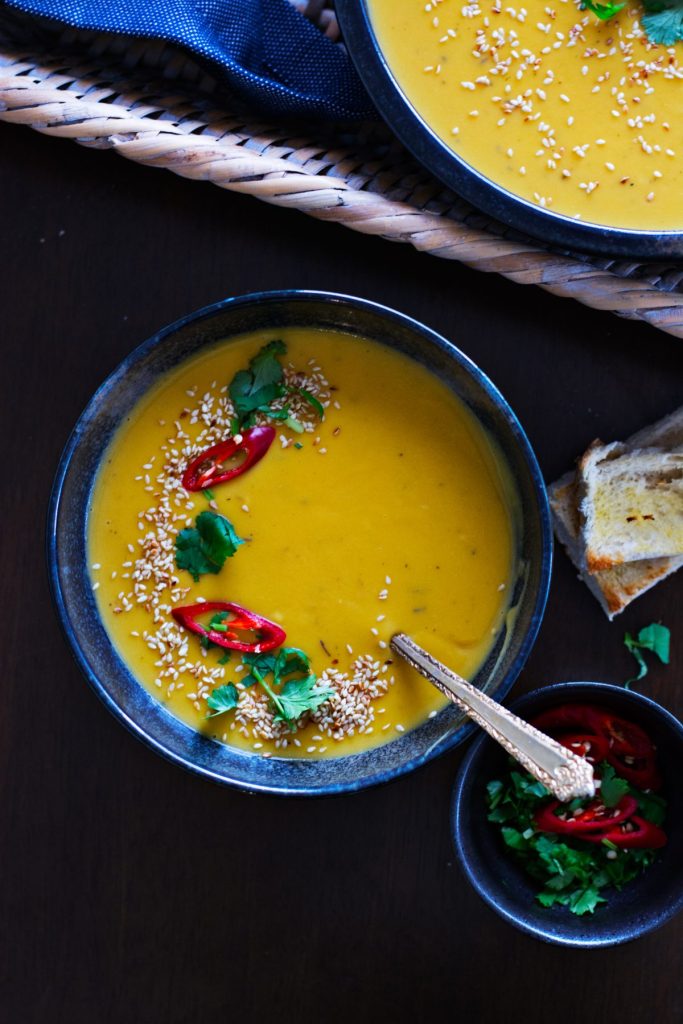 Pumpkin and potato soup garnished with sesame seeds and red chillies served in black bowl