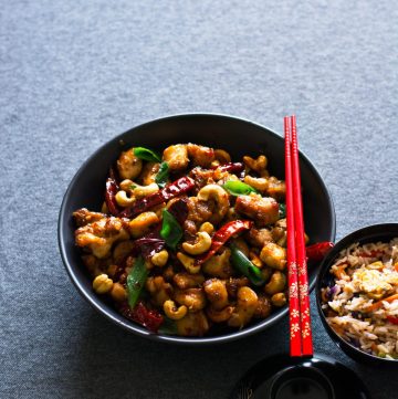 Chicken stir fry with sichuan peppercorns served in a black bowl with red chopsticks on top