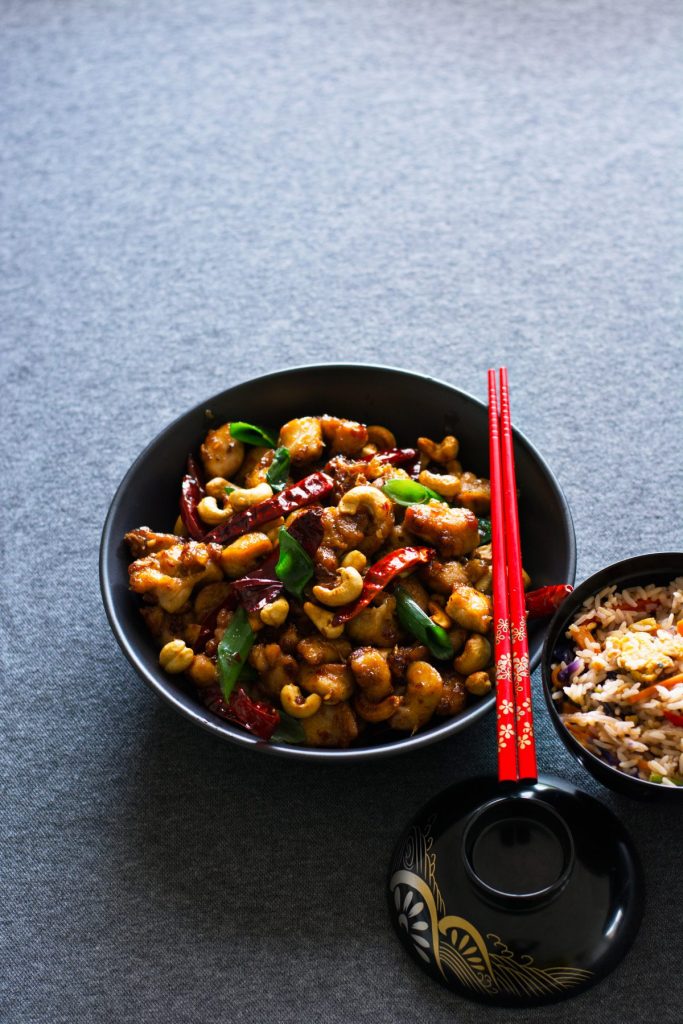 Chicken stir fry with sichuan peppercorns served in a black bowl with red chopsticks on top