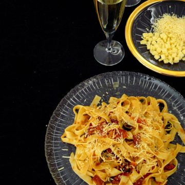 Pasta with tomatoes served on plate with cheese and a glass of wine in the background