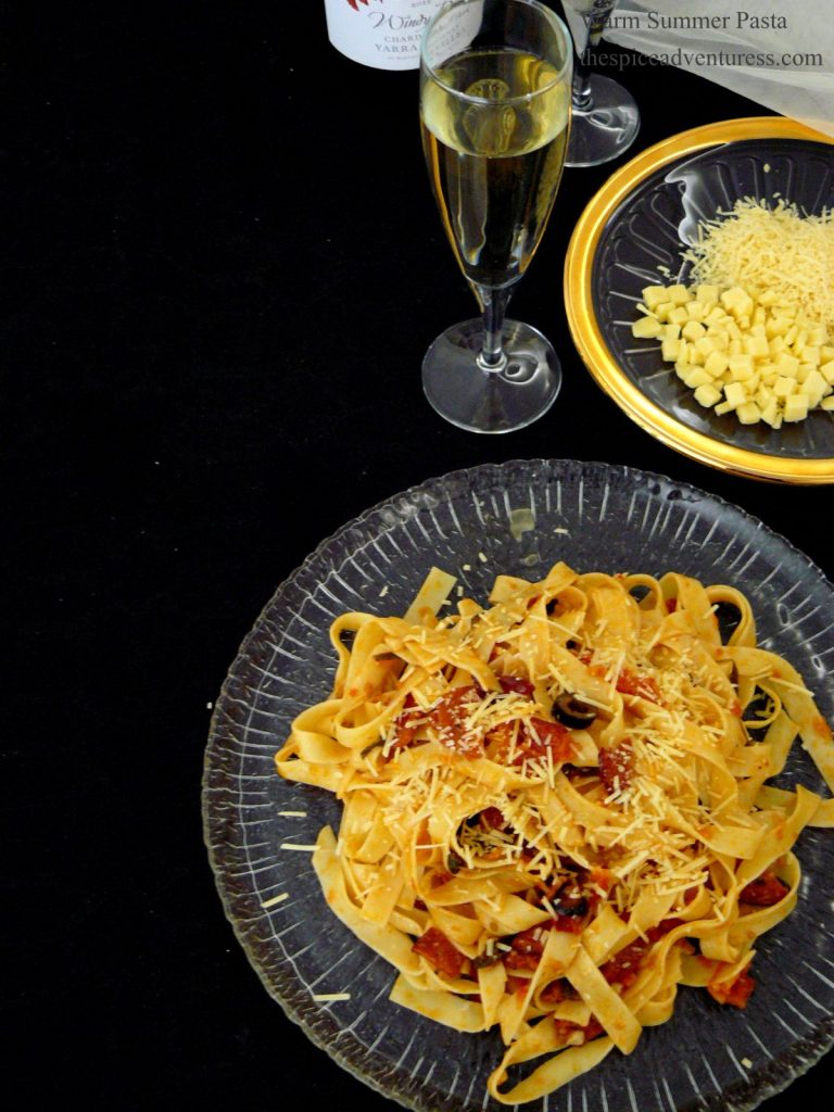 Pasta with tomatoes served on plate with cheese and a glass of wine in the background