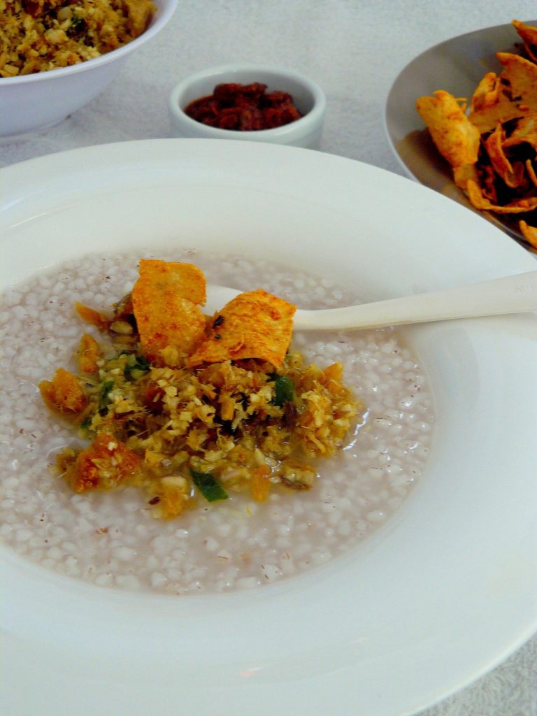 Rice gruel topped with dry shark chutney and pappadums served in white bowl