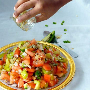 Hand pouring dressing over tomato salad