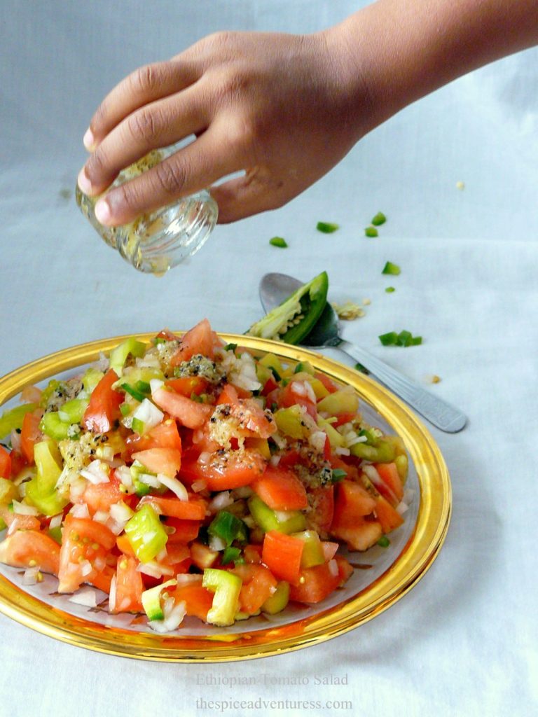 Hand pouring dressing over tomato salad