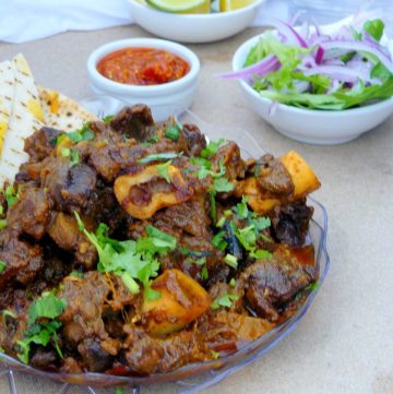 Lamb curry served on plate with salad and lemon wedges on the side