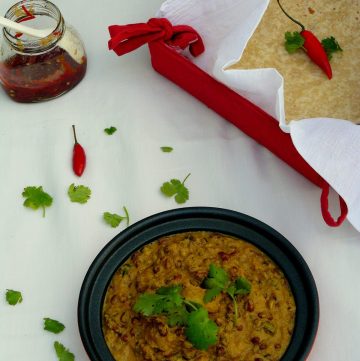 Adzuki beans and potato curry served in black bowl with flatbreads on the side